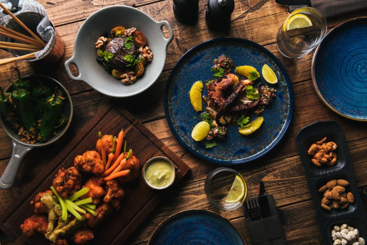 Five Jumeirah Village Dubai Exterior foto The photo displays a beautifully arranged spread of various dishes on a wooden table. 

1. In the center, there's a blue plate featuring a main dish garnished with lemon slices and fresh herbs.
2. To the left, another dish includes fried pieces, like