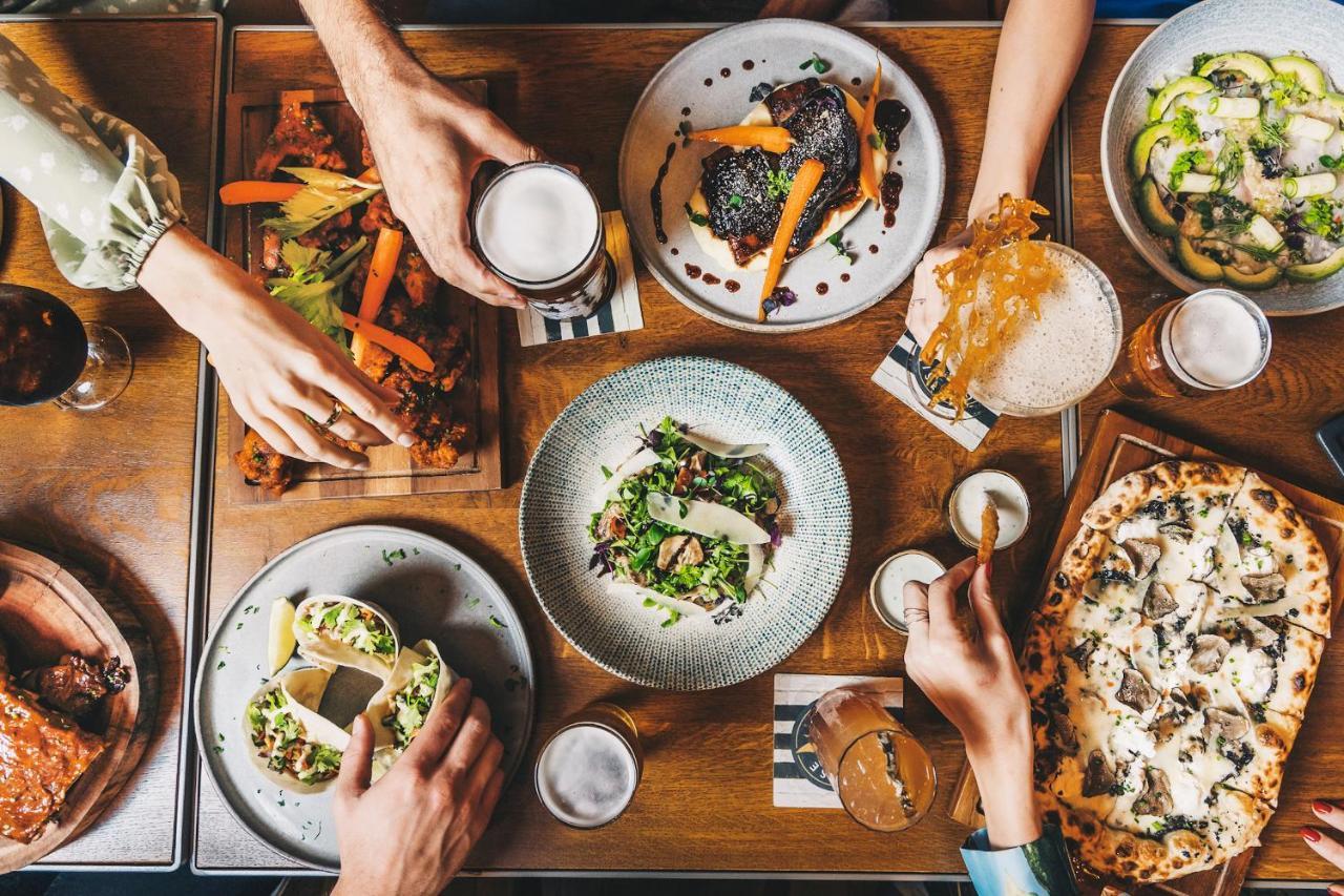 Five Jumeirah Village Dubai Exterior foto The photo displays a table filled with a variety of delicious food and drinks. There are several dishes, including a colorful salad in a round bowl, tacos, and what appears to be a pizza. On the side, there are also wooden platters with grilled veget
