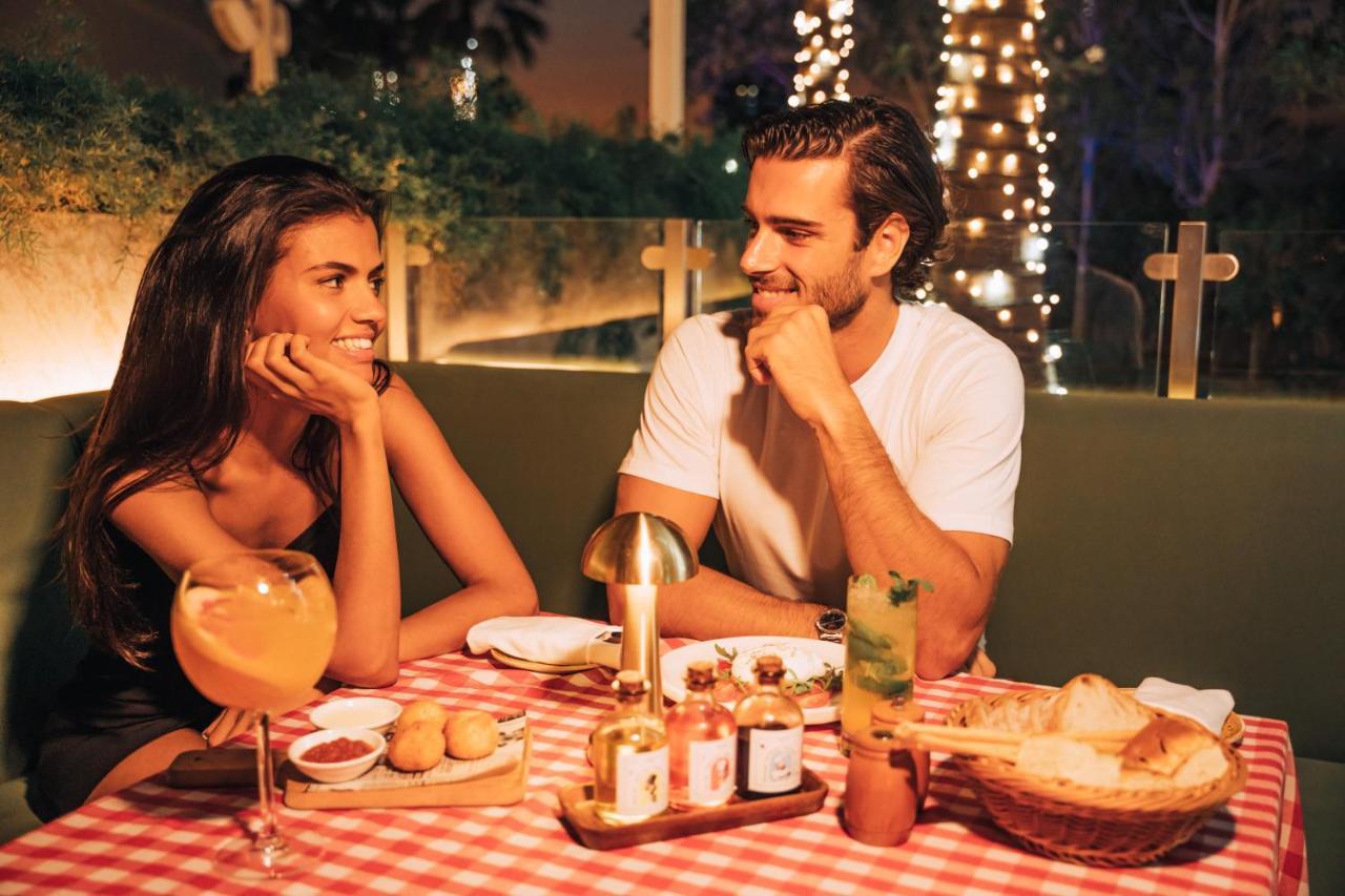 Five Jumeirah Village Dubai Exterior foto The photo shows a romantic dining scene featuring a couple at a table. The setting is illuminated with soft lights, creating a warm atmosphere. The table is adorned with a red and white checkered tablecloth, and various dishes are presented, includin
