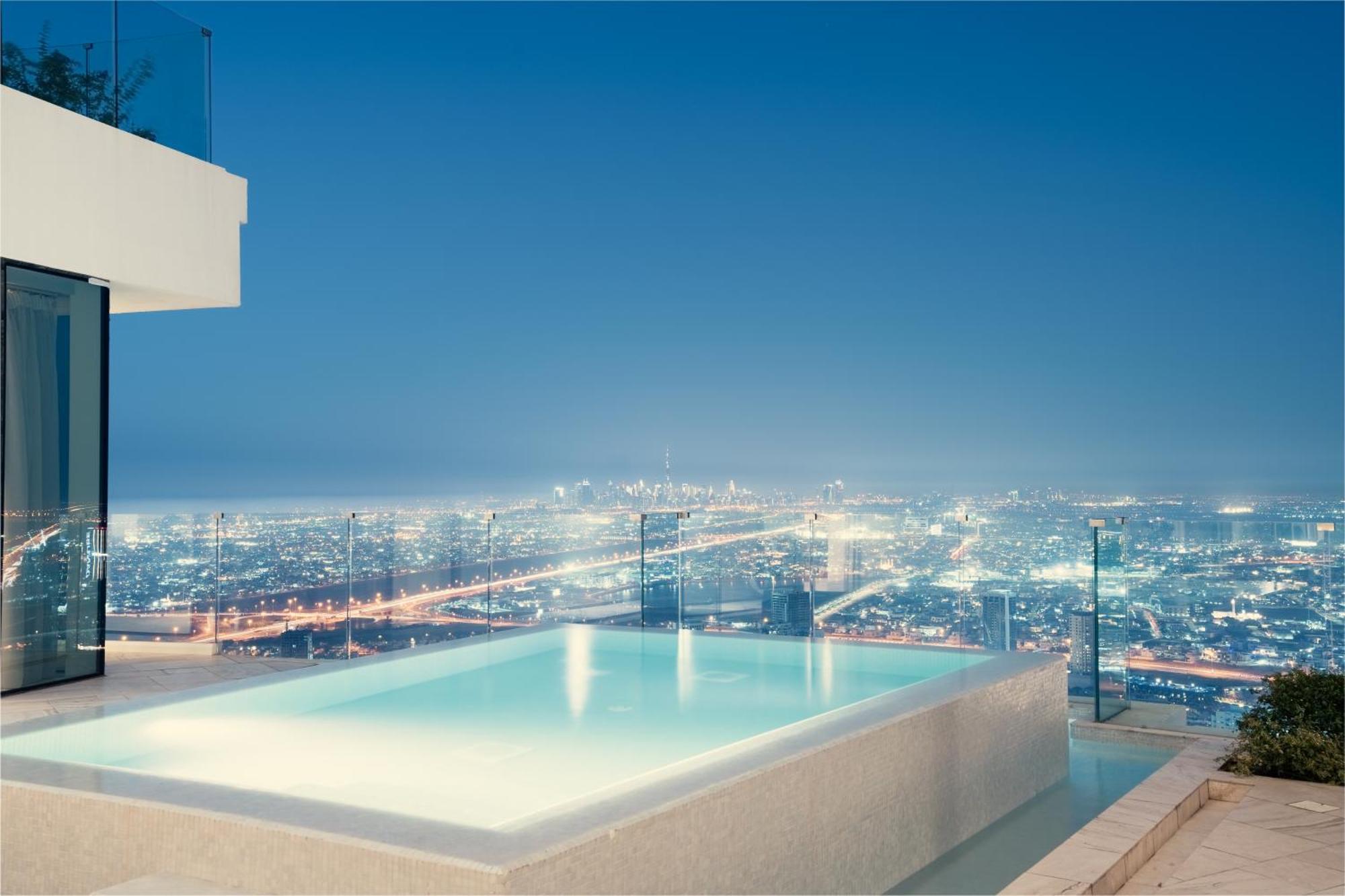 Five Jumeirah Village Dubai Exterior foto The photo showcases a luxurious infinity pool situated on an elevated terrace, overlooking a sprawling cityscape at night. The pool's water has a serene glow, reflecting the city lights below, which shimmer and create a vibrant backdrop. The architec