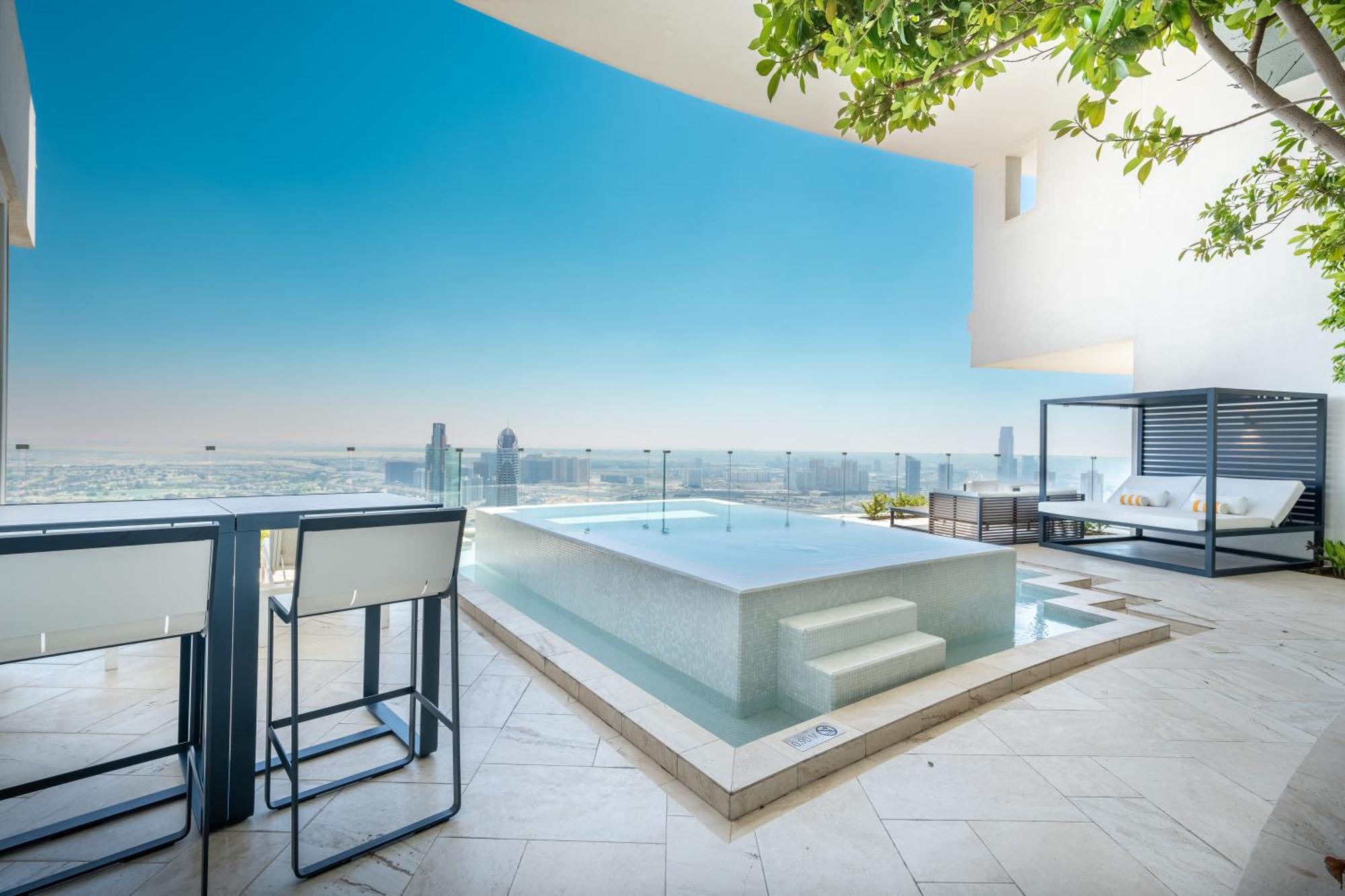 Five Jumeirah Village Dubai Exterior foto The photo shows a modern outdoor space featuring a sleek infinity pool. The pool appears to be situated on a terrace with a stunning view of a city skyline or landscape in the background. There are elegant lounge chairs and a shaded cabana area, crea