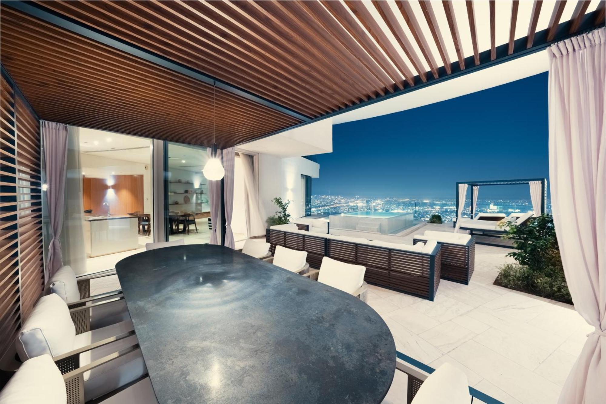 Five Jumeirah Village Dubai Exterior foto The photo shows a modern outdoor dining area with a sleek, curved table surrounded by several chairs. It features a stylish wooden ceiling with slats, creating a shaded atmosphere. In the background, large glass doors lead to the interior of a house,