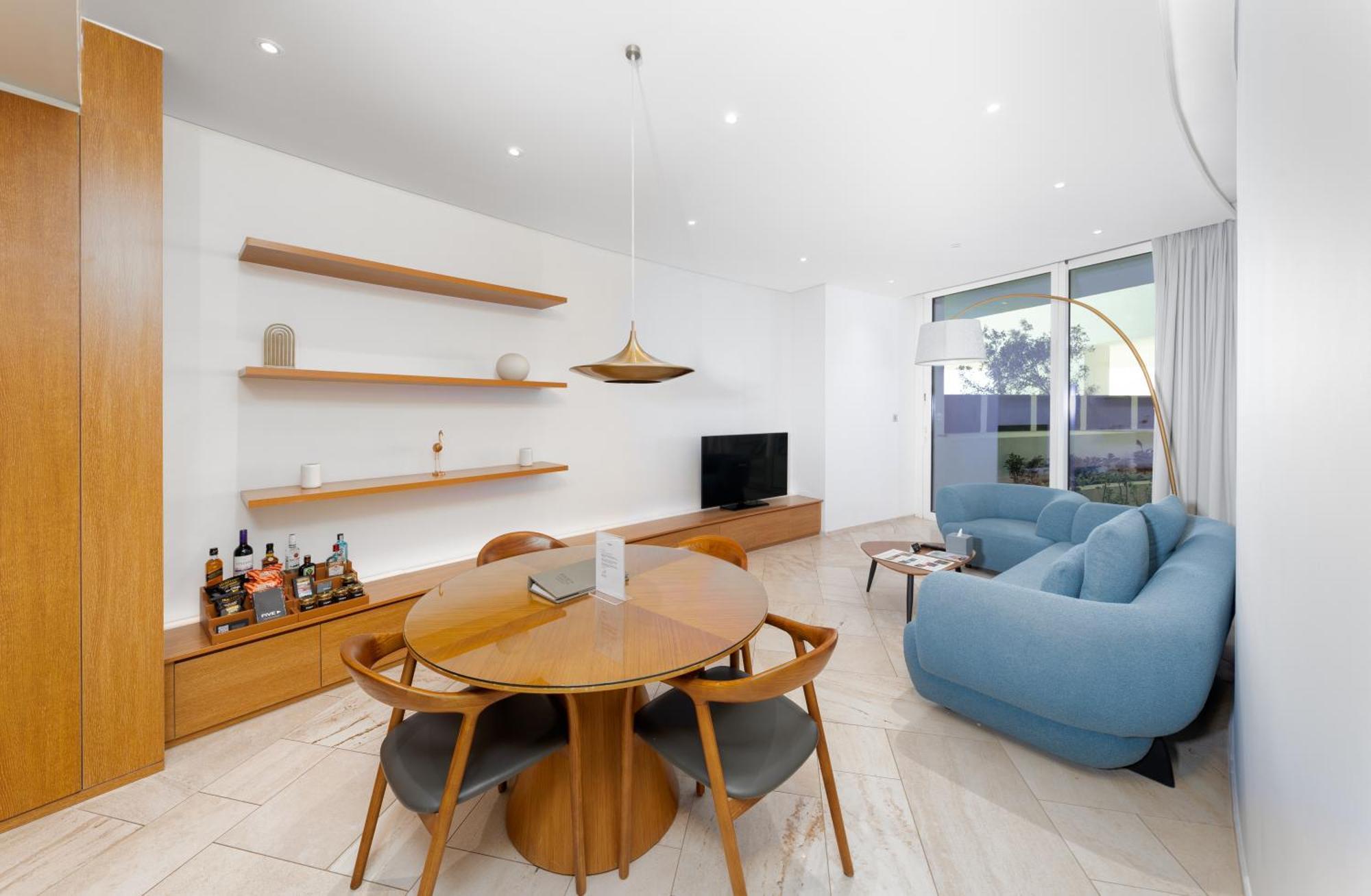 Five Jumeirah Village Dubai Exterior foto The image shows a modern living space that features a cozy and stylish design. On one side, there is a round wooden dining table surrounded by four chairs. The table is set with a small item, possibly a decorative piece or a book. 

A pendant light h