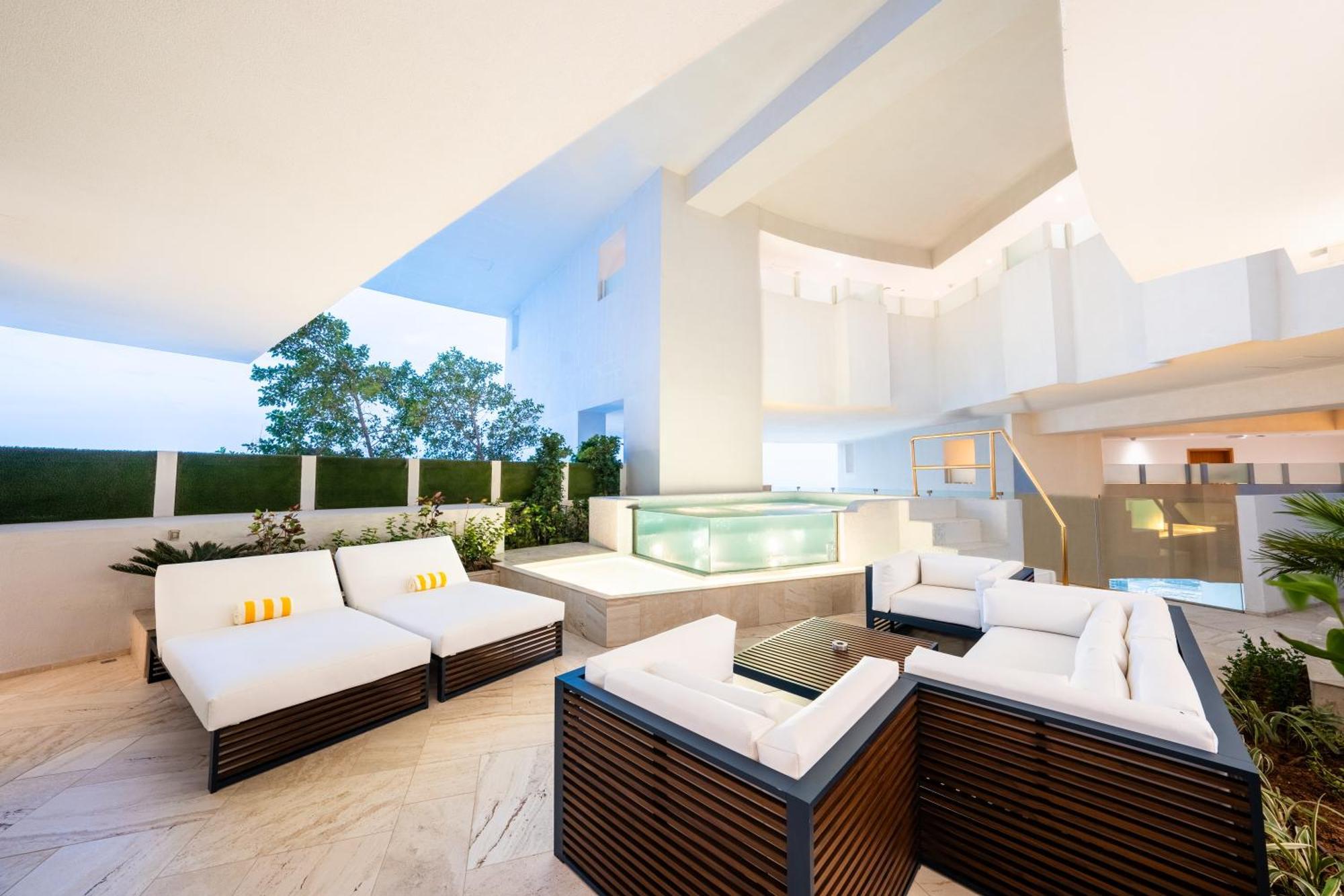 Five Jumeirah Village Dubai Exterior foto The photo depicts a modern outdoor lounge area featuring comfortable seating arrangements. There are several white sofas with dark wooden frames, arranged around a glass coffee table. In the background, there is a sleek water feature or pool, surroun