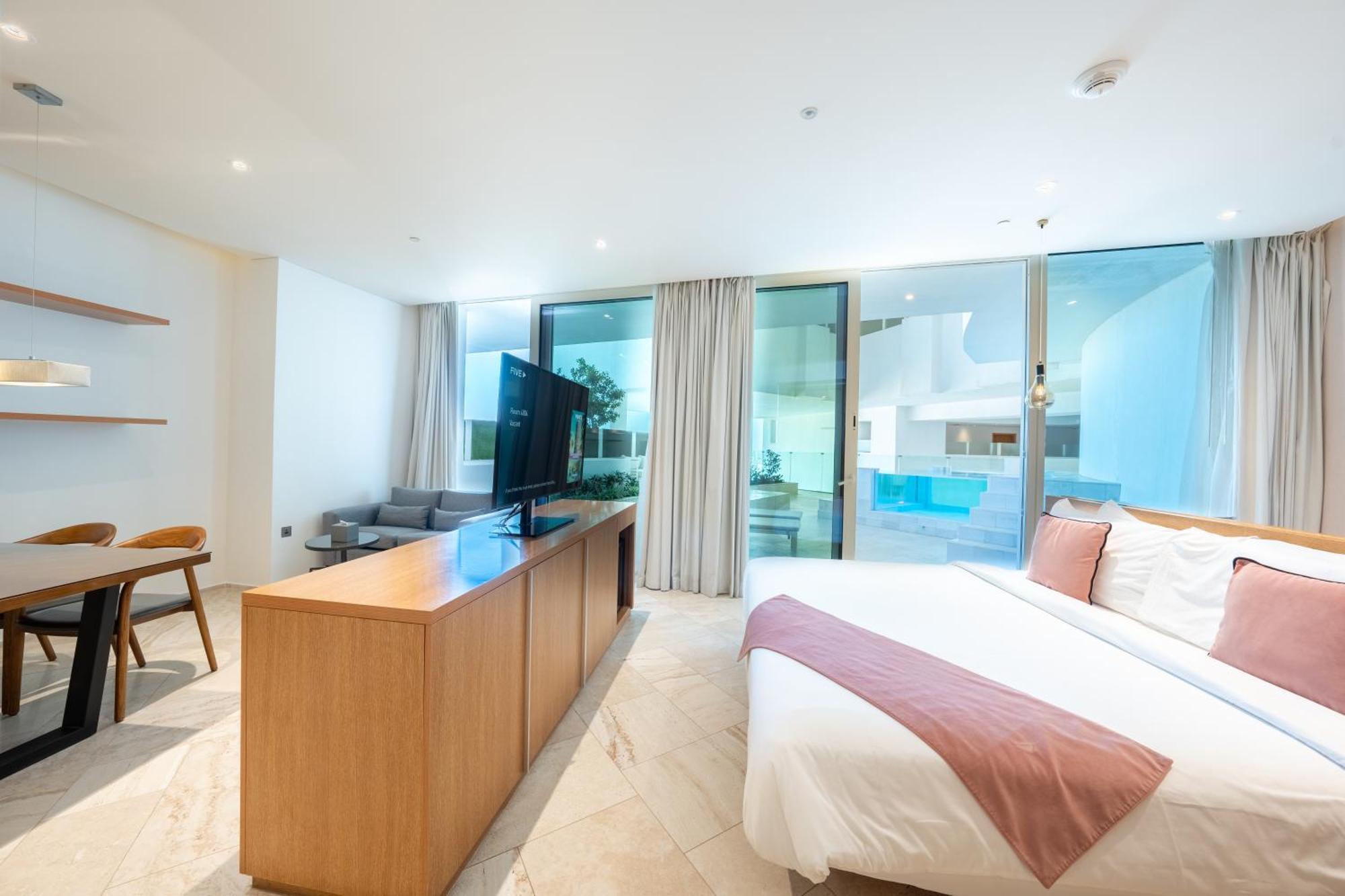 Five Jumeirah Village Dubai Exterior foto The photo shows a modern hotel room or a studio apartment. It features a large window with sheer curtains, allowing natural light to fill the space. There’s a double bed with a white bedspread and a light pink throw blanket at the foot. Opposite the 