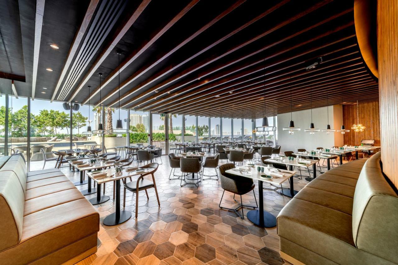 Five Jumeirah Village Dubai Exterior foto The photo shows the interior of a modern restaurant. It features a spacious layout with a combination of wooden and tiled flooring, characterized by hexagonal tiles. The ceiling has a modern design with wooden beams that add a sophisticated touch. Th